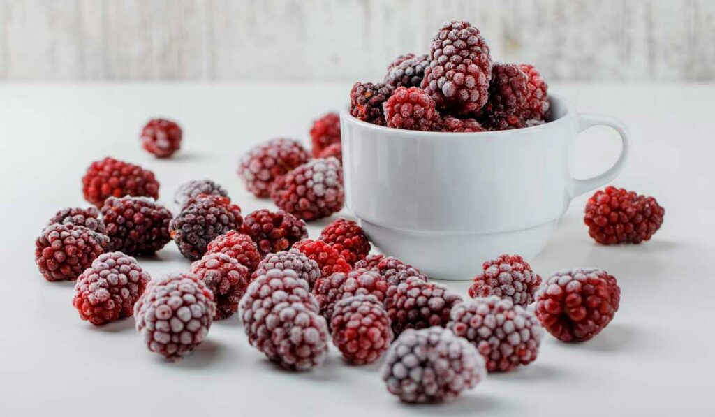 Amoras numa xícara e frutos espalhados sobre a mesa