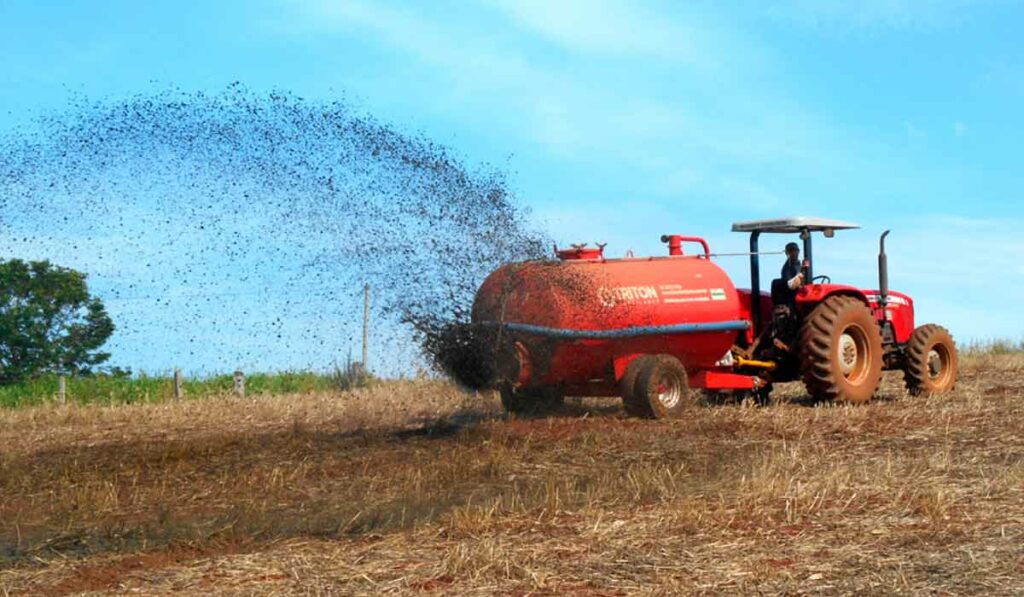 Agricultor distribuindo adubo orgânico na lavoura utilizando um tanque tracionado por trator