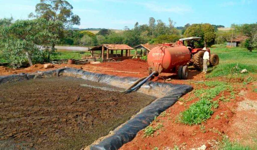 Esterqueira construída com geomembrana e agricultor abastecendo tanque de adubo orgânico para distribuição na lavoura ou pastagem