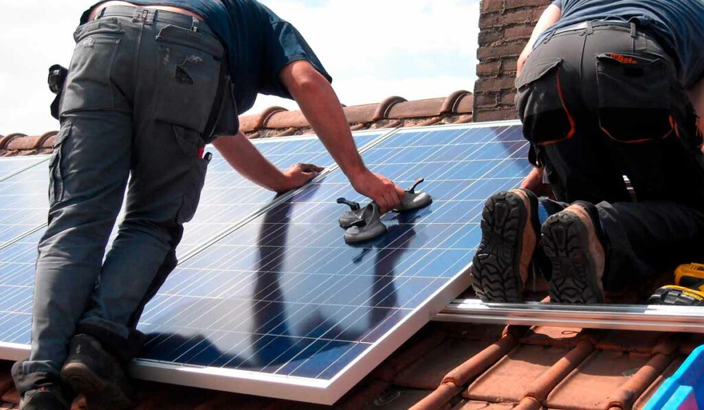 Homens instalando sistema de energia solar sobre o telhado de uma residência