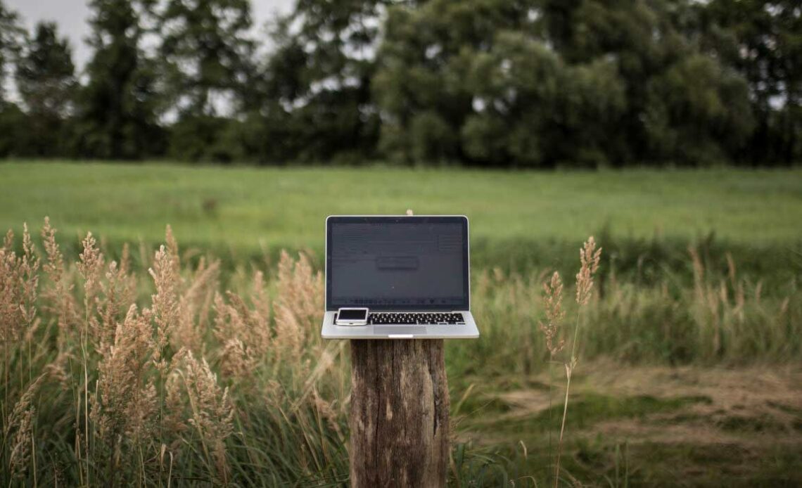 Internet rural - laptop e celular sobre um moirão na área rural