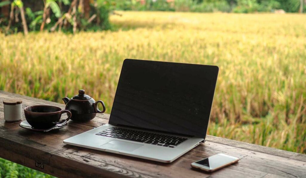Laptop e celular no guarda corpo da varanda da sede da fazenda com bule e caneca de café