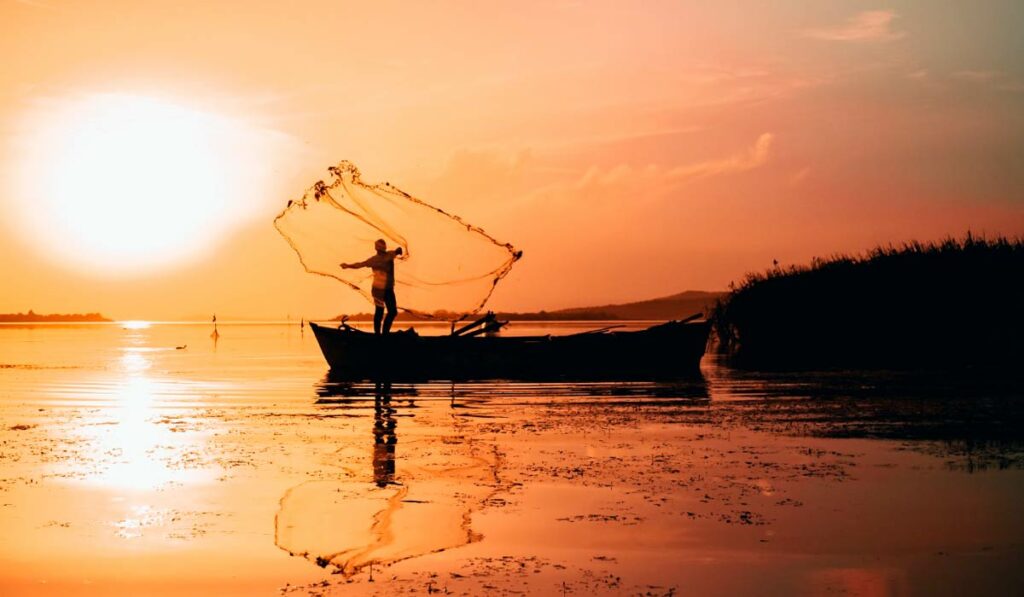 Pescador no seu barco jogando a tarrafa com o nascer do sol ao fundo