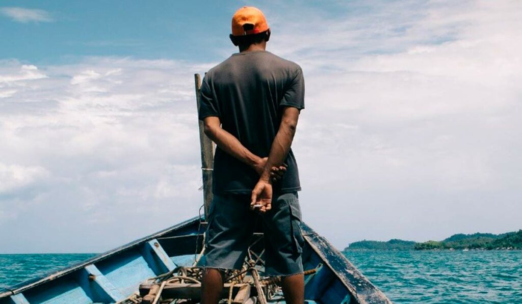 Pescador na proa de seu barco atuando como vigia - espiando a ocorrência de cardumes