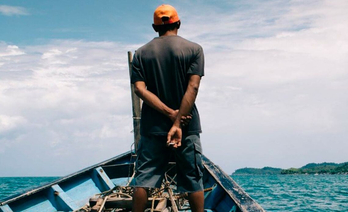 Pescador na proa de seu barco atuando como vigia - espiando a ocorrência de cardumes