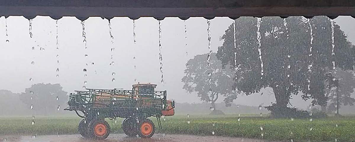 Chuva na fazenda com máquina agrícola ao fundo
