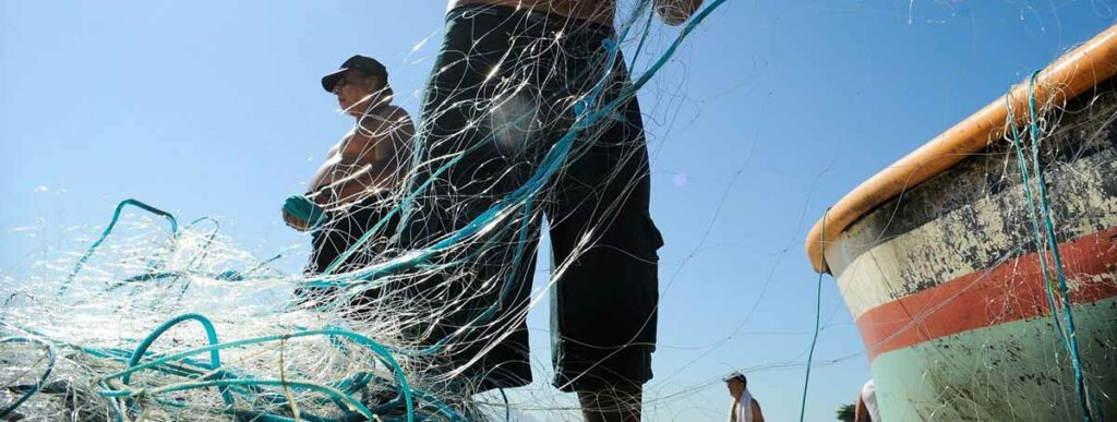Pescadores artesanais preparando a rede de pesca na praia junto ao barco