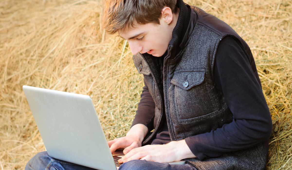 Jovem rural sentado no celeiro com feno e um laptop