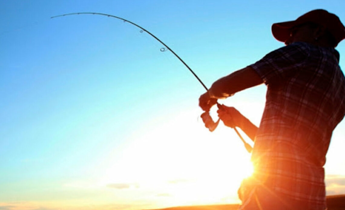 Pescador praticando a pesca com vara e molinete e sol ao fundo da paisagem