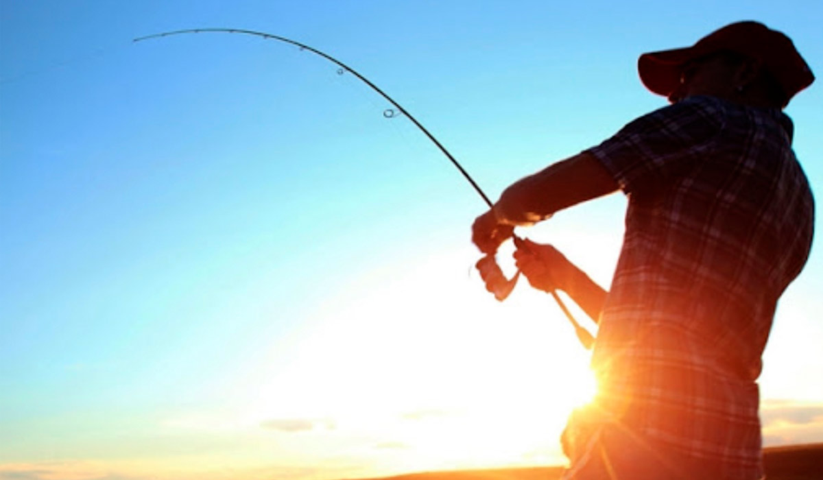 Pescador praticando a pesca com vara e molinete e sol ao fundo da paisagem