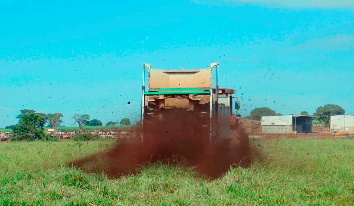 Máquina realizando operação de adubação orgânica em pastagem com composto avícola