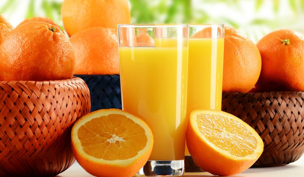 Copos de suco de laranja com frutos em cestas sobre a mesa