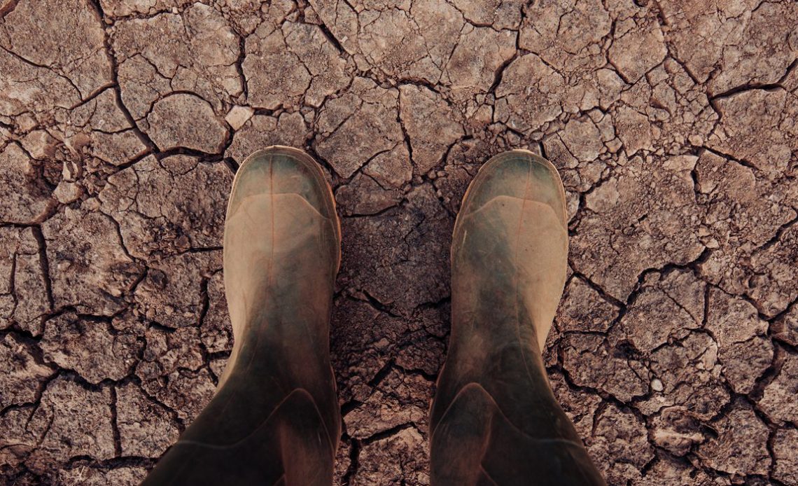 Agricultor pisando com suas botas de borracha sobre o solo esturricado