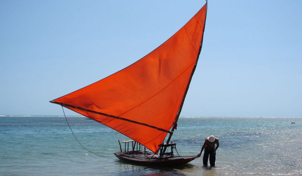 Jangada com vela vermelha e jangadeiro em praia do Ceará