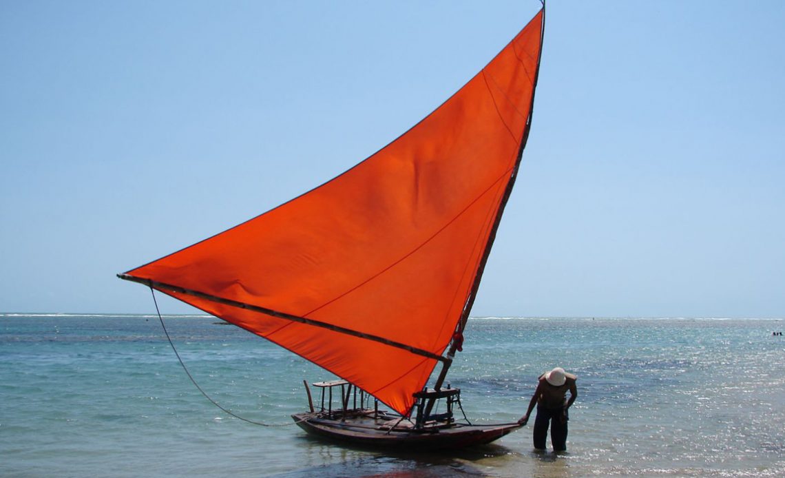 Jangada com vela vermelha e jangadeiro em praia do Ceará