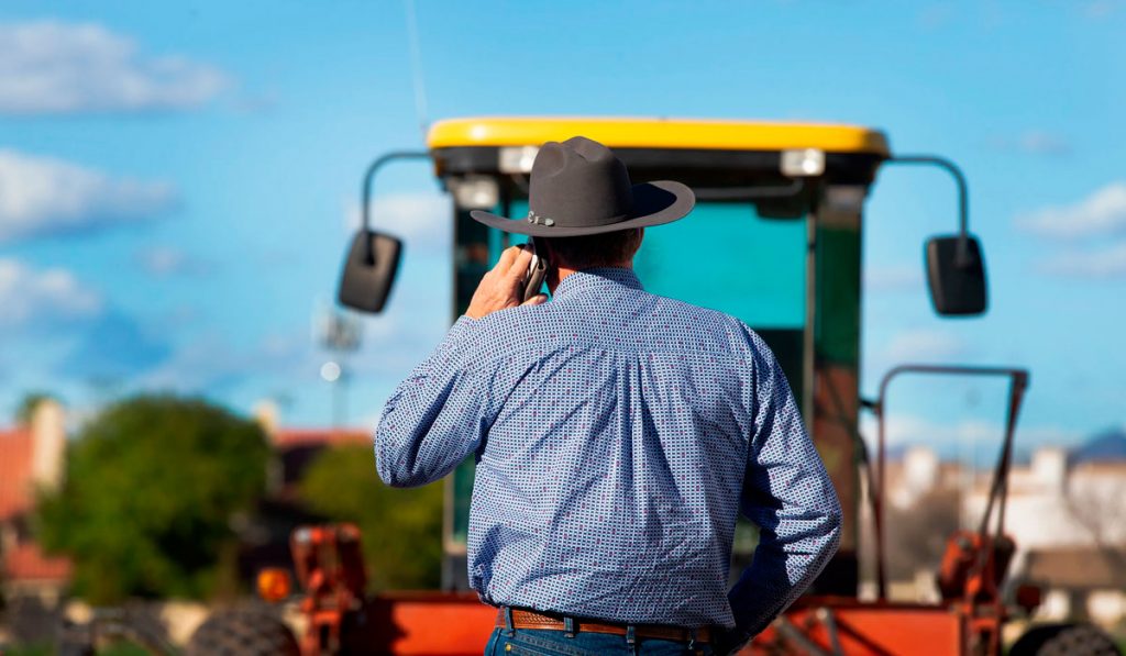 Agricultor ao celular monitorando operação com máquina no campo