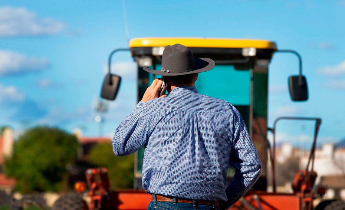 Agricultor ao celular monitorando operação com máquina no campo