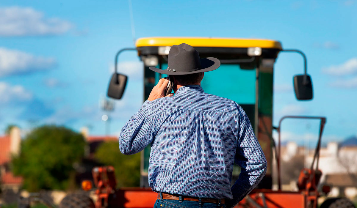 Agricultor ao celular monitorando operação com máquina no campo