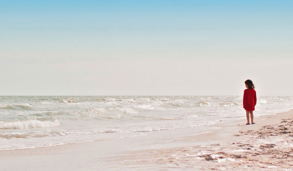 Menina na praia contemplando a imensidão do oceano à sua frente