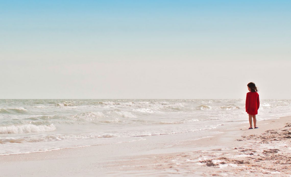 Menina na praia contemplando a imensidão do oceano à sua frente