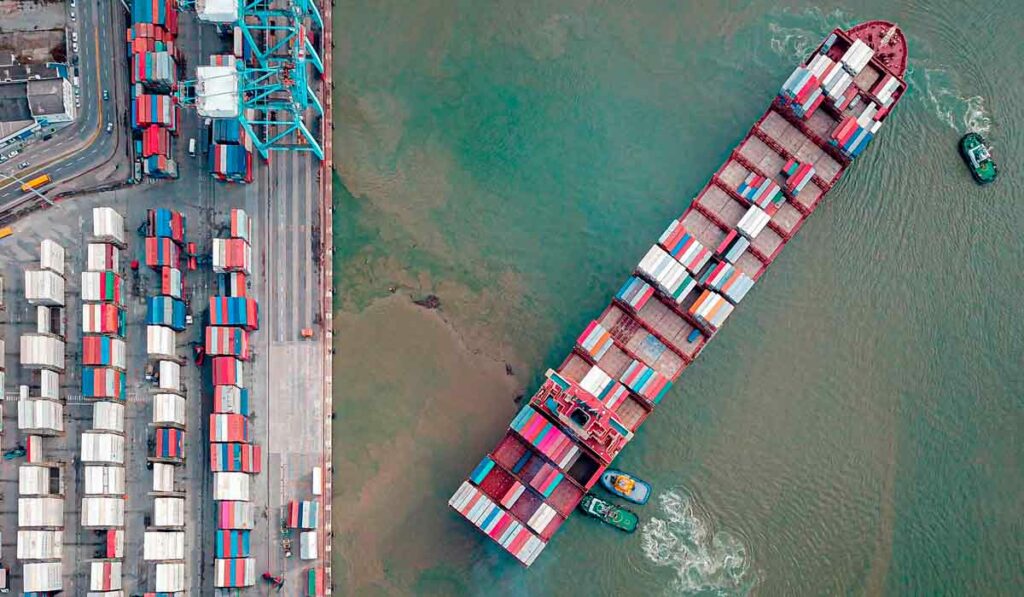 Navio carregado com containeres sendo desatracado do porto