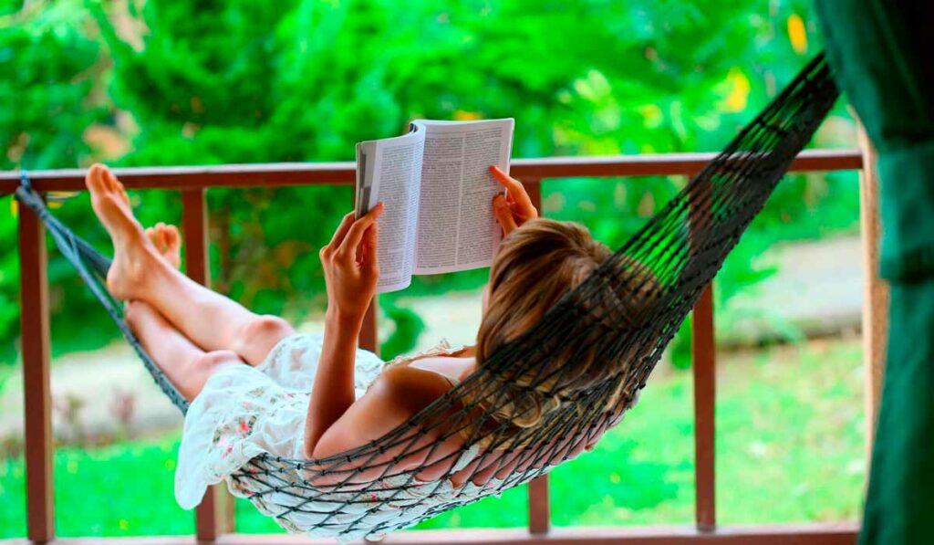 Produtora rural lendo um livro na rede na varanda de sua casa na fazenda
