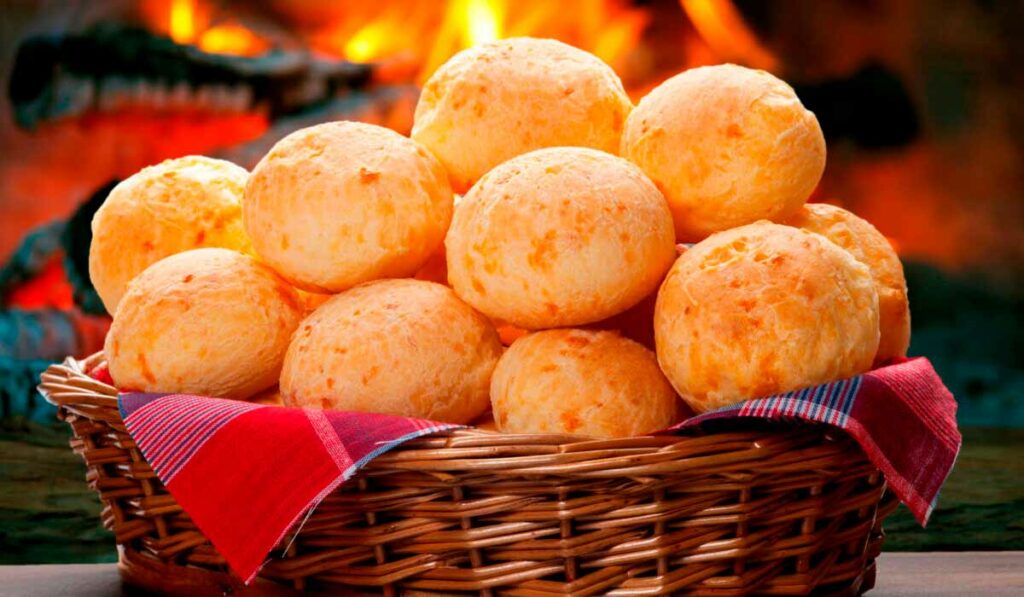 Cesto com pães de queijo sobre a mesa e fogo do forno a lenha ao fundo