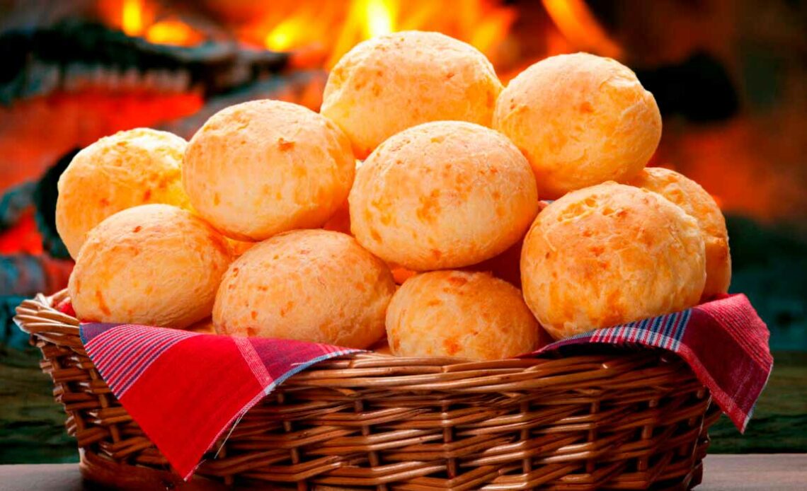 Cesto com pães de queijo sobre a mesa e fogo do forno a lenha ao fundo