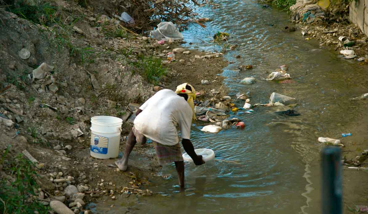 Pessoa coletando água em riacho poluído