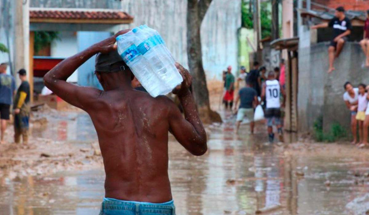 Homem carregando galões de água em ocupação desordenada sem saneamento
