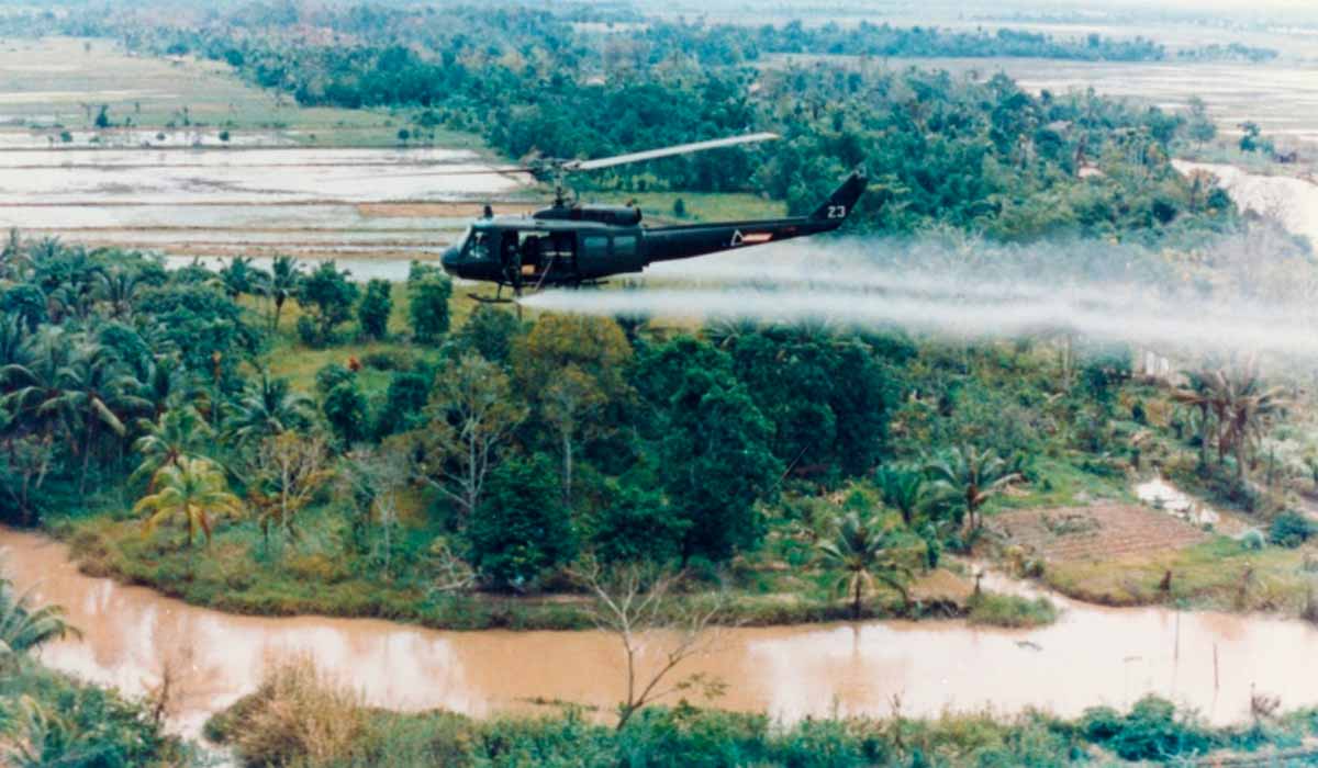 Um helicóptero UH-1D espalhando agente laranja em uma floresta no Vietnã