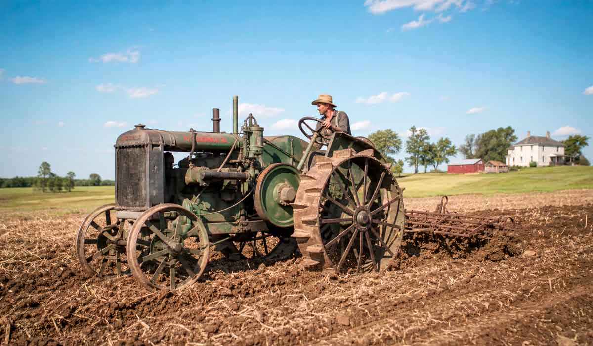 O termo trator, derivado de máquina de tracionar, consolidou-se no mercado a partir de 1906. Trator vintage dos anos 1910 com rodas de ferro e garras, em cena rural histórica O termo trator, derivado de máquina de tracionar, consolidou-se no mercado a partir de 1906. Trator vintage dos anos 1910 com rodas de ferro e garras, em cena rural histórica